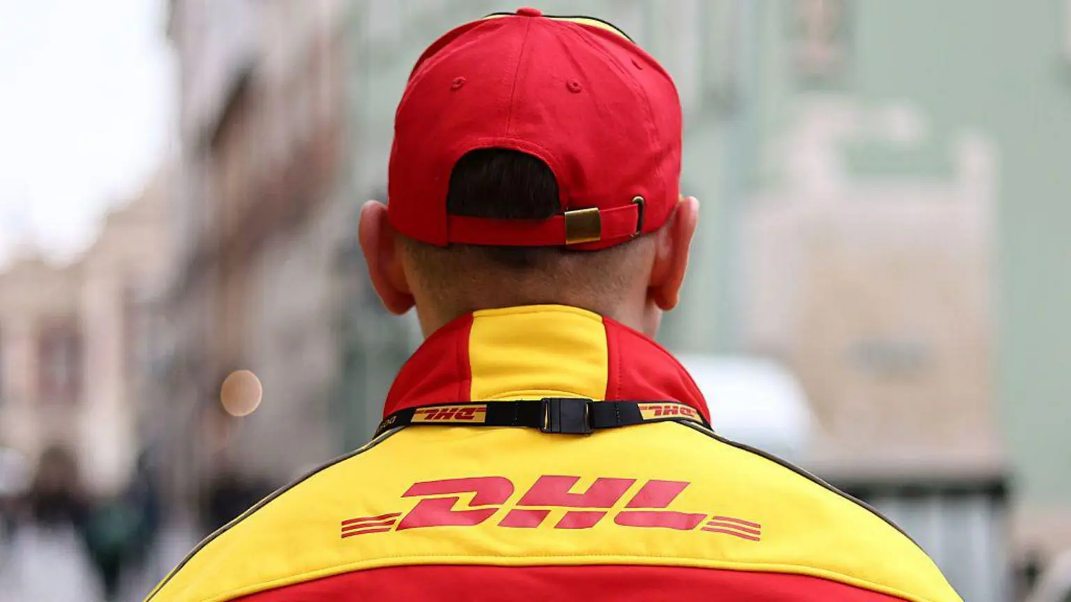 Чоловік-працівник DHL у жовто-червоній фірмовій куртці в червоній кепці