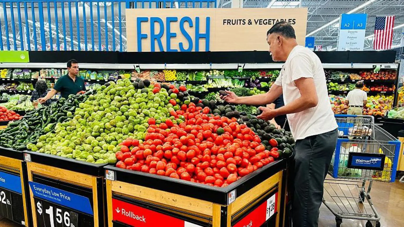 Чоловік у білій футболці тримає авокадо, стоячи в відділі продуктів перед купою помідорів, авокадо та інших овочів у Walmart у Розміді, Каліфорнія, 11 квітня 2025 року.