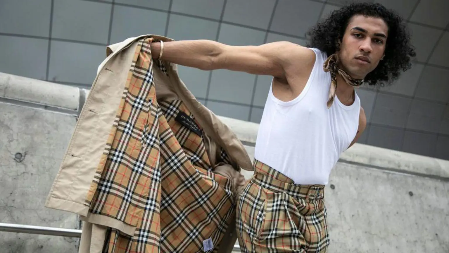 Чоловік знімає свій плащ Burberry, щоб показати відповідні брюки Burberry у клітинку