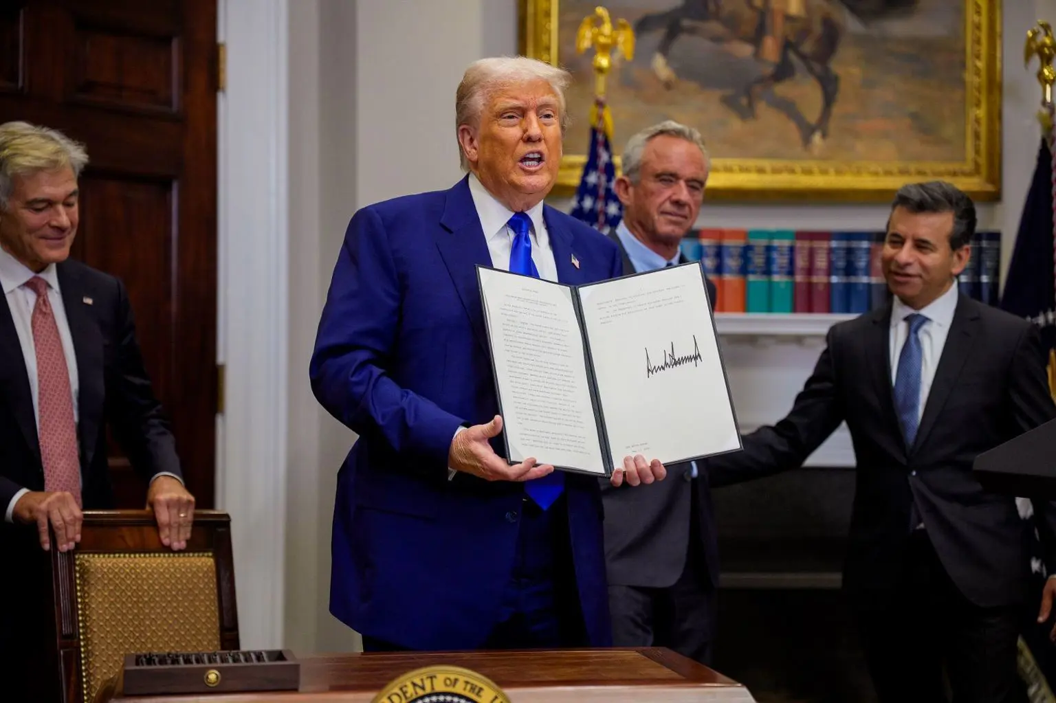 Президент США Дональд Трамп тримає свій виконавчий наказ, а представники охорони здоров’я дивляться на нього: (зліва направо) адміністратор Medicare і Medicaid Мехмет Оз, міністр охорони здоров’я Роберт Кеннеді-молодший і комісар Управління з контролю за продуктами й ліками Мартін Макарі