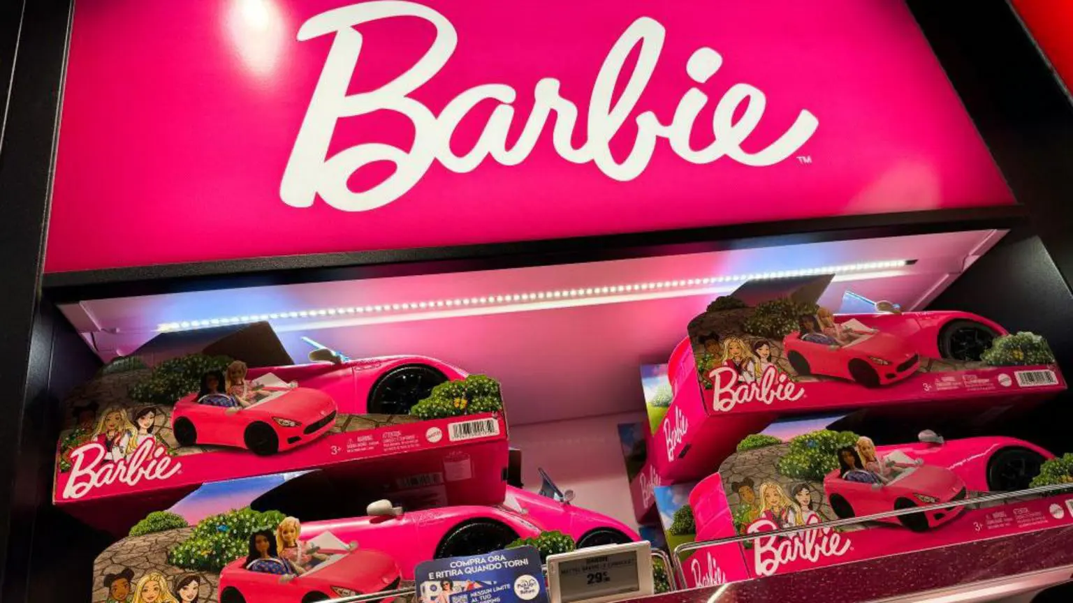 Машинки Барбі на виставці в торговій точці. Білий логотип Barbie розташований над іграшками на яскраво-рожевому фоні.