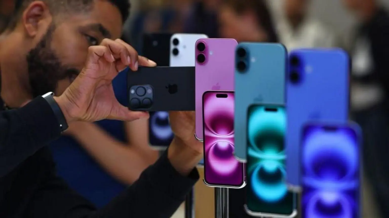 Чоловік дивиться на iphone, виставлені в синьо-зеленому та фіолетовому кольорах