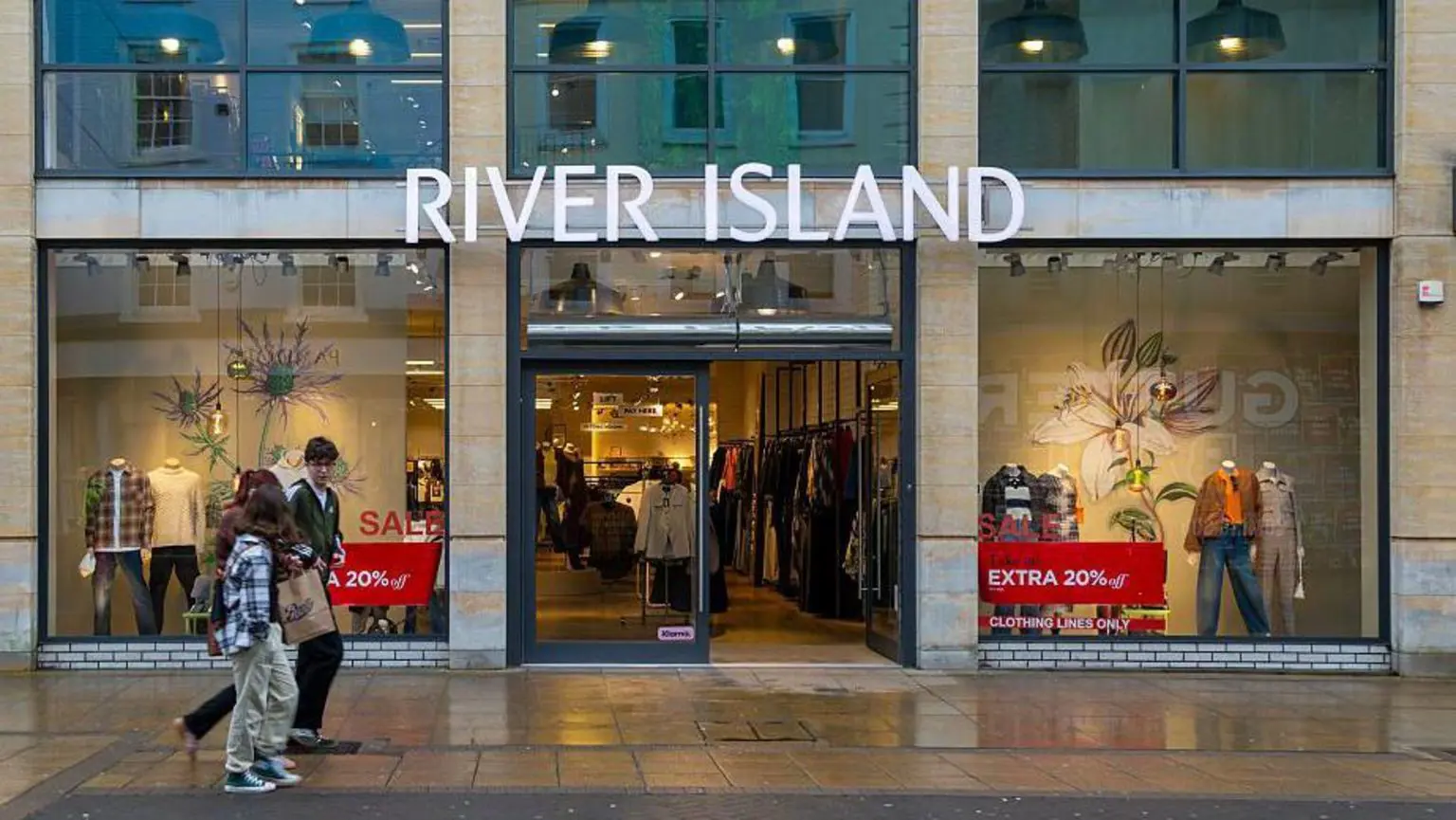 Група молодих людей проходить повз магазин River Island із рекламними табличками у вітрині