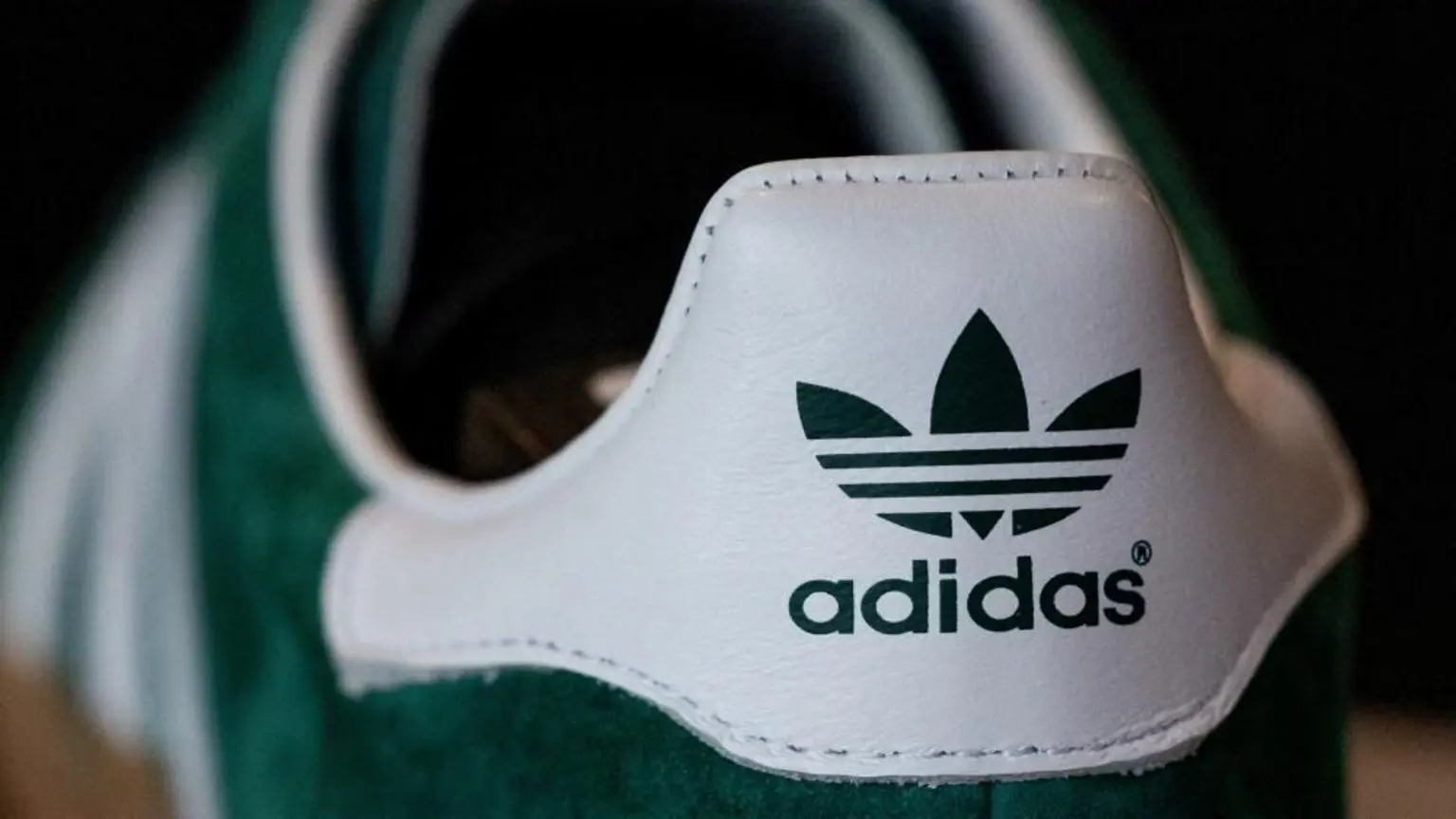 Зелено-білі кросівки крупним планом із великим логотипом Adidas на п’яті.
