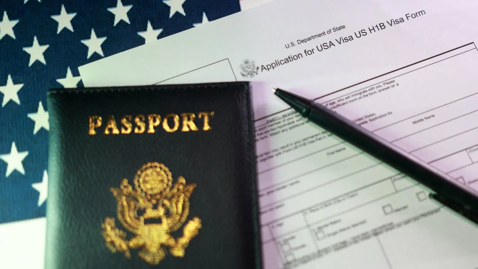 Заява на отримання візи H-1B лежить на столі поруч із паспортом США та чорною ручкою.