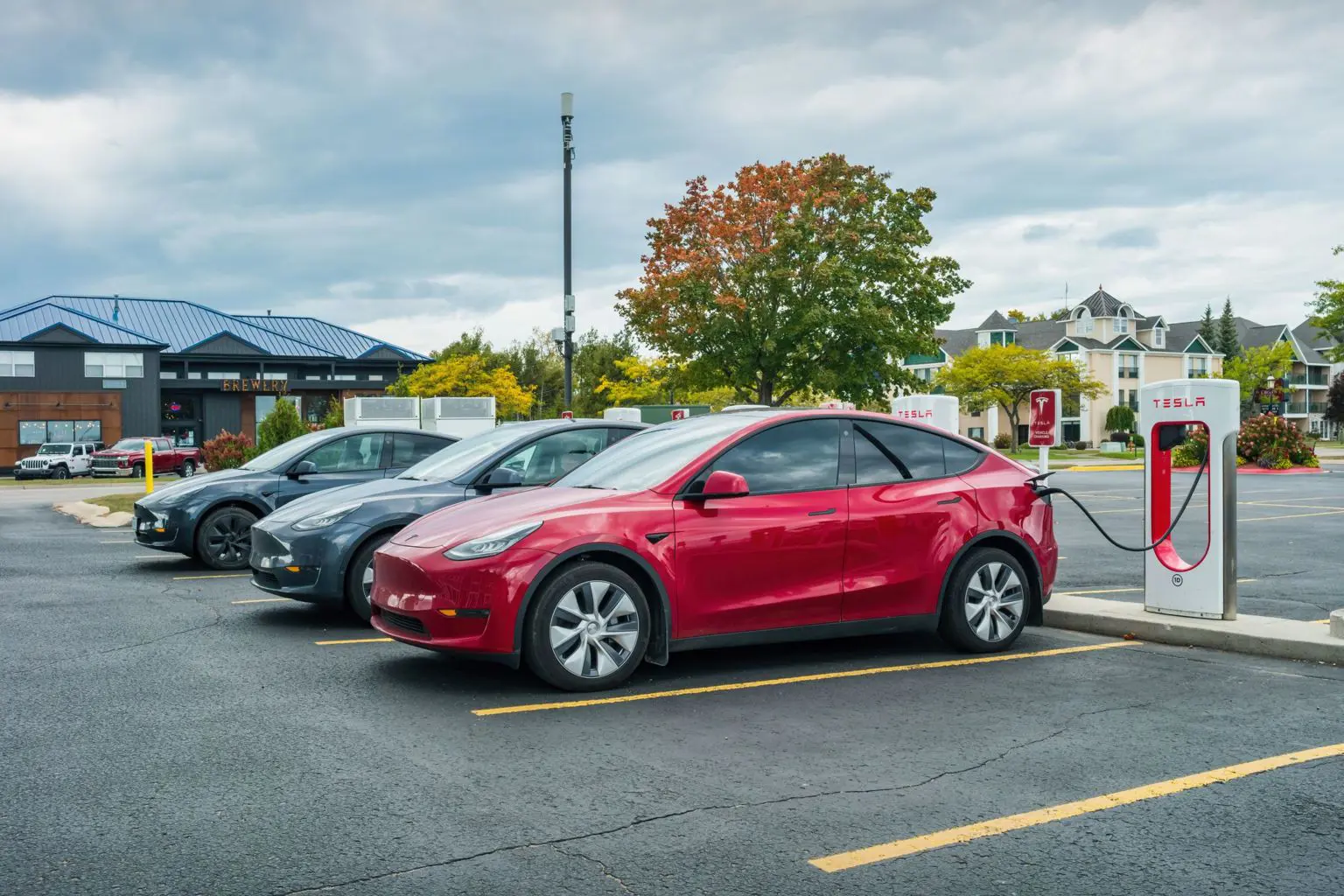 Червоний автомобіль Tesla заряджається на зарядній станції Tesla на парковці.