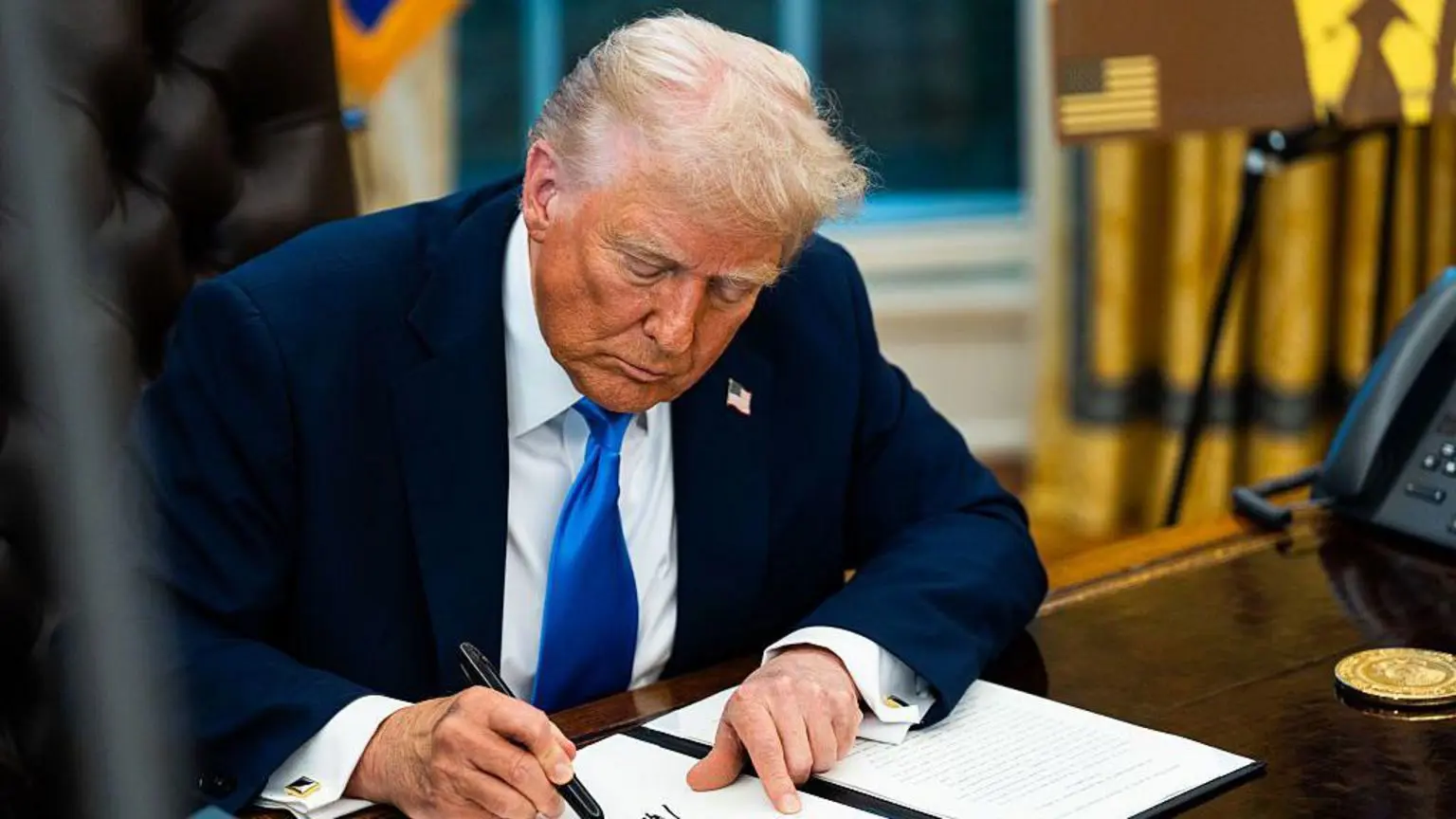 Дональд Трамп сидить за столом Resolute Desk в Овальному кабінеті та підписує виконавчий указ про візу для кваліфікованих працівників.