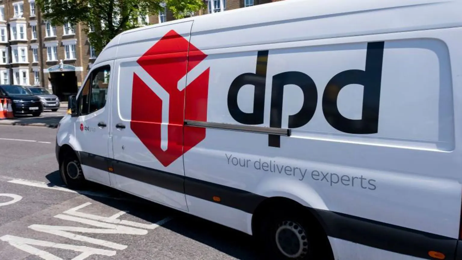 Фургон DPD виїжджає на дорогу в сонячний день, а на задньому плані видно будинки