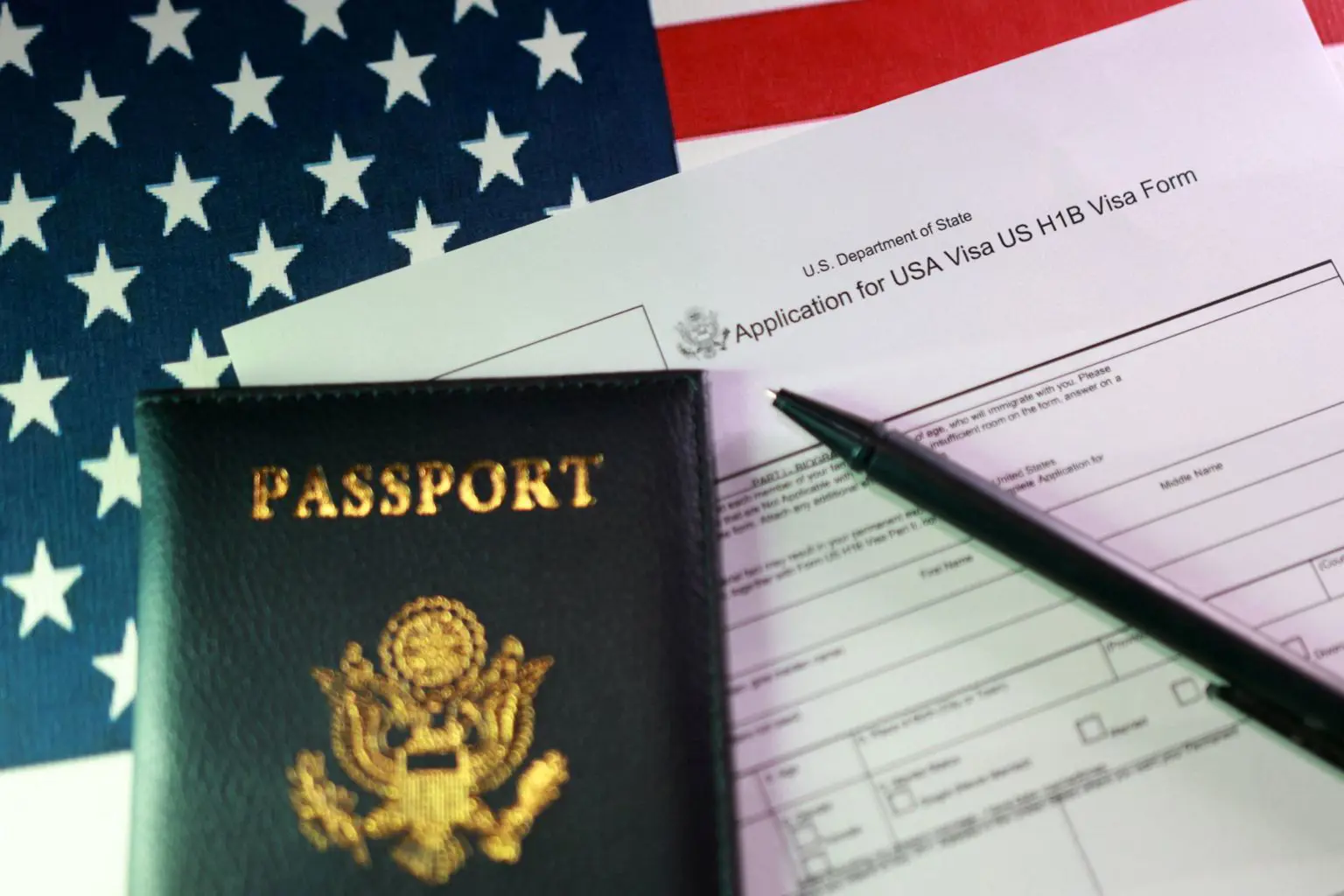 Заява на отримання візи H-1B лежить на столі поруч із паспортом США, ручкою та американським прапором.