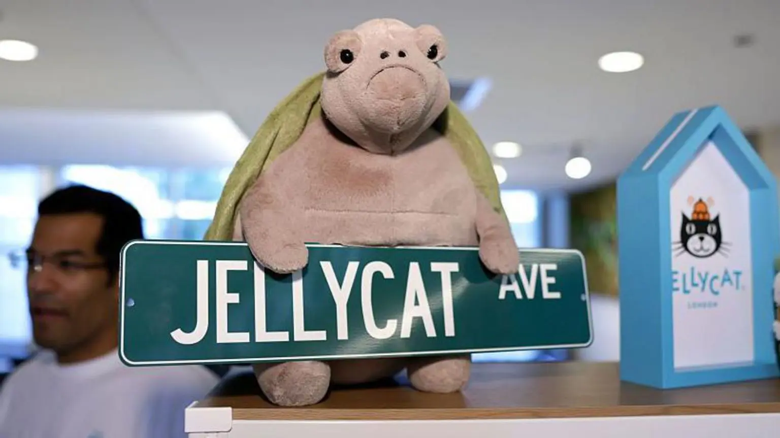 М'яка іграшка Черепаха Jellycat із сумним виразом обличчя сидить на полиці з табличкою з написом Jellycat