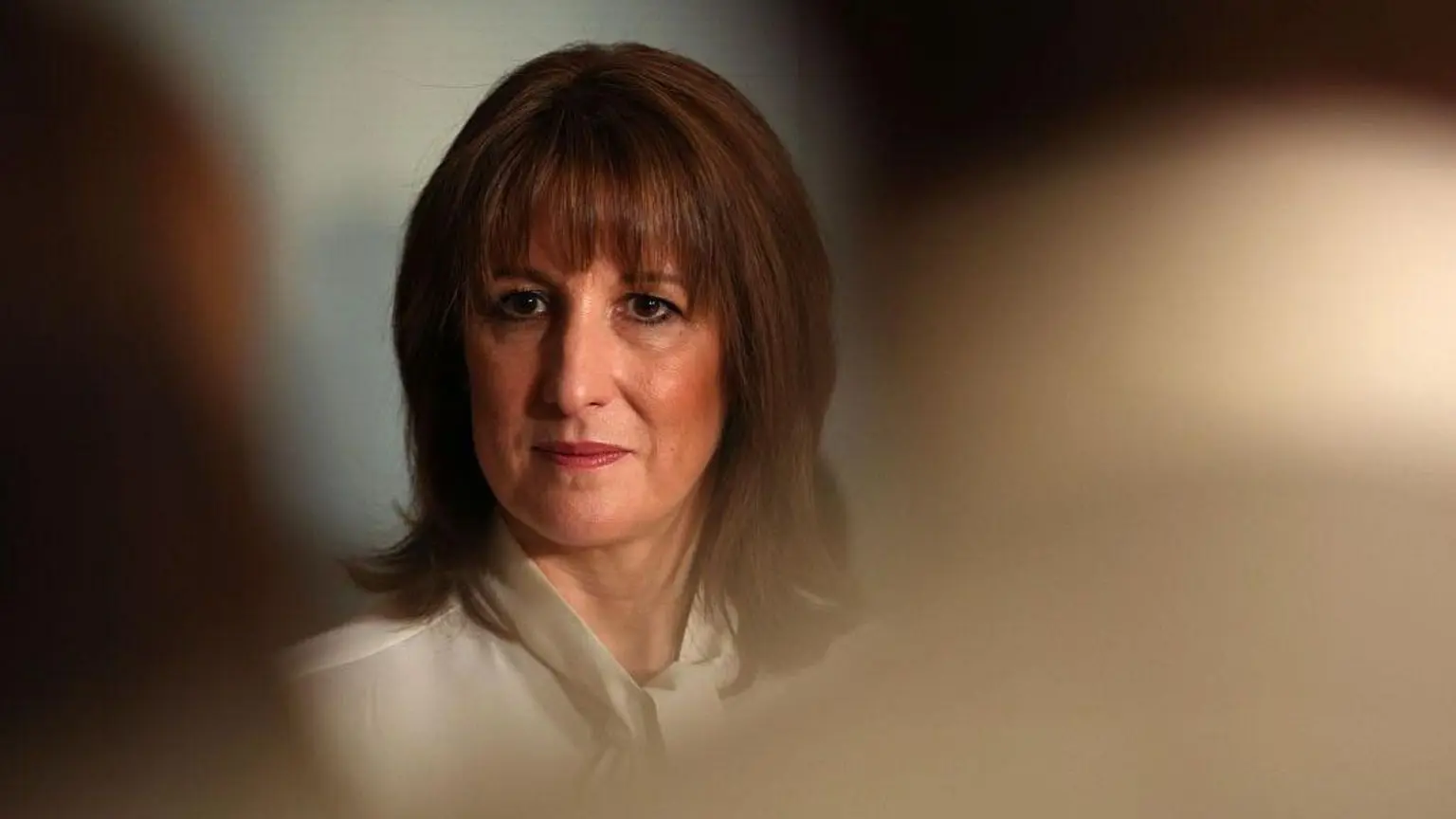 Рейчел Рівз, одягнена в білу блузку, можна побачити у фокусі між головами аудиторії