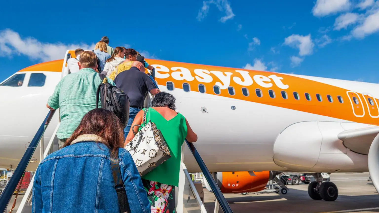 Люди піднімаються сходами на помаранчево-білий літак easyJet.