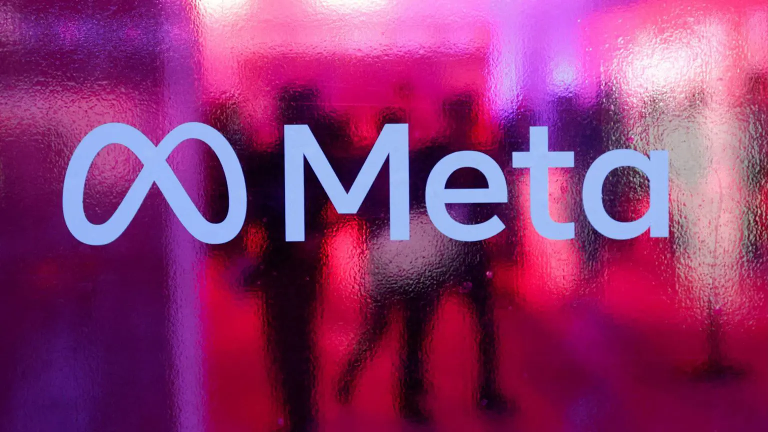 Логотип Meta зображено на рожевому матовому склі. За логотипом зображено силуети людей.
