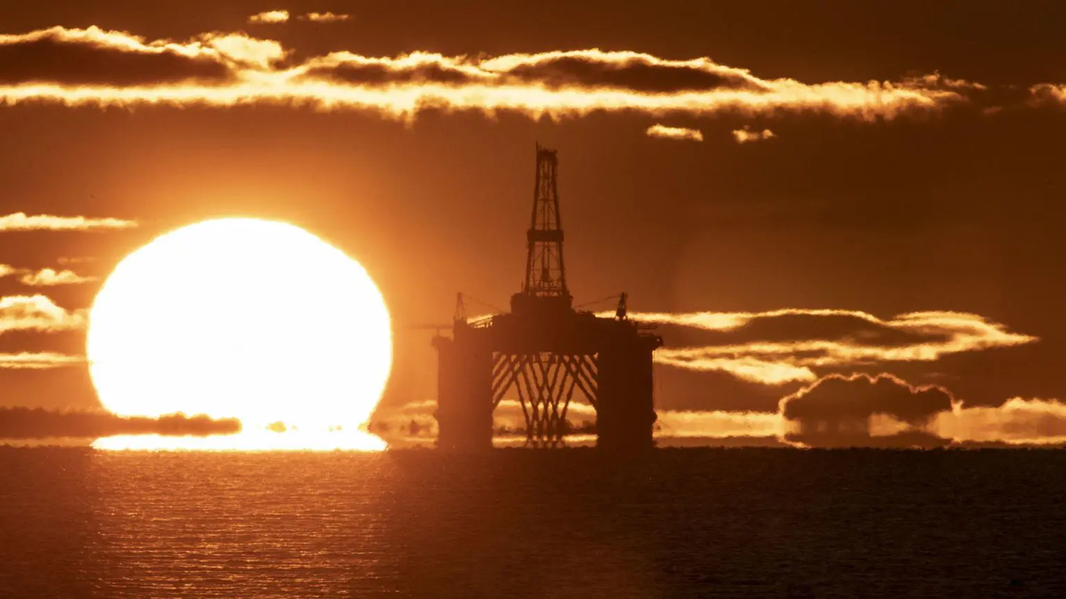 Сонце на горизонті за нафтогазовою платформою в Північному морі. Море спокійне, і весь пейзаж яскраво-помаранчевого кольору.