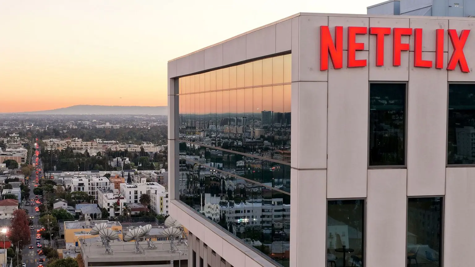 Широкий ракурс показує логотип Netflix на стіні кремової будівлі студії Netflix у 2025 році в Лос-Анджелесі, на тлі культового горизонту Лос-Анджелеса на заході сонця.
